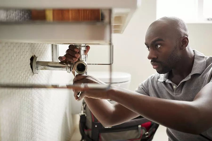 Plumbing-Contractor-Insurance-Closeup-of-a-Male-Plumber-Sitting-on-the-Floor-and-Fixing-a-Bathroom-Sink