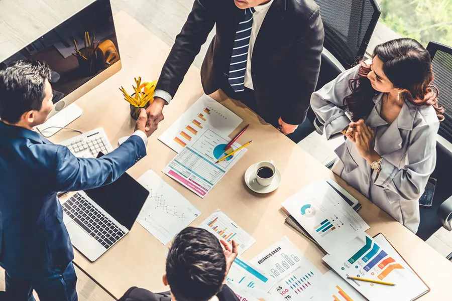 Our Comprehensive Approach - Two Businessmen Shaking Hands Across Table During a Business Meeting in a Modern Office